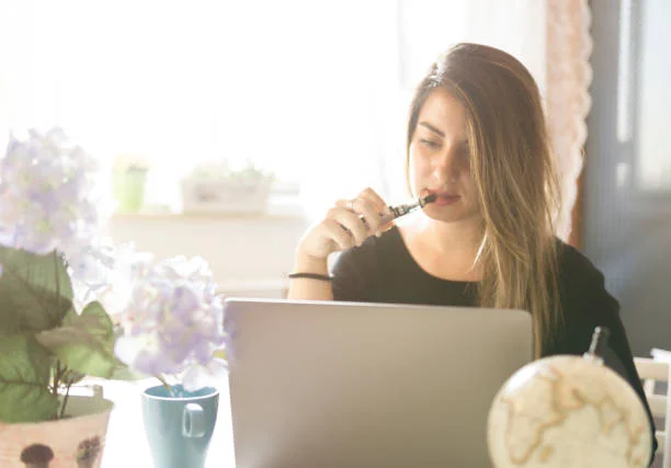 A woman taking a vape break beside her laptop.