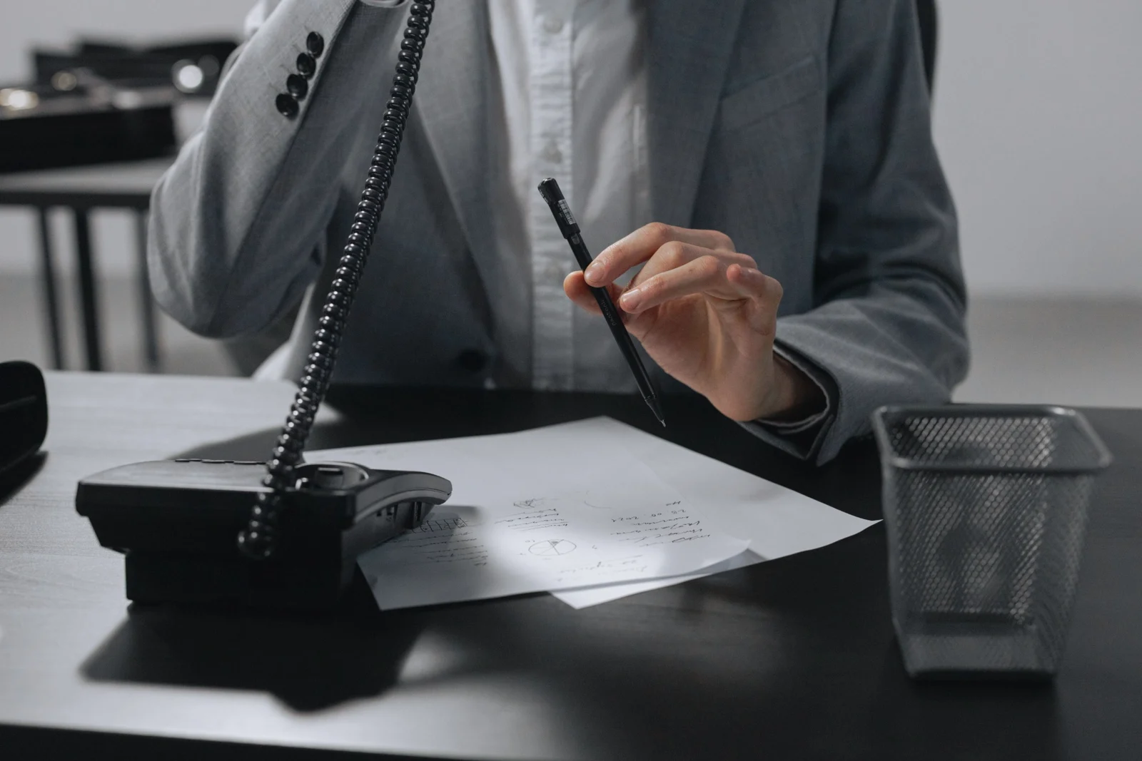 A person taking a phone call at a desk, with a pen and notes ready.